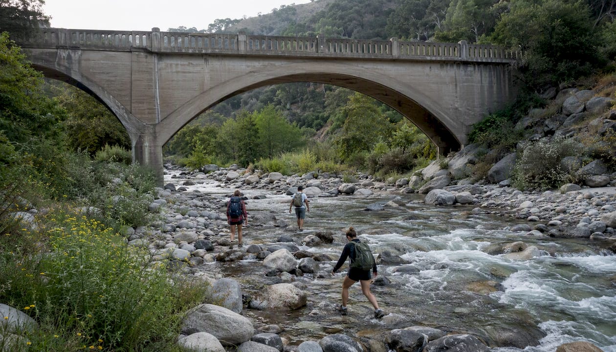 Hikers crossing river by Bridge to Nowhere on weekend