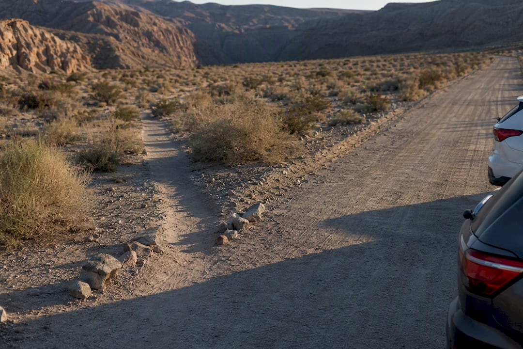 Unmarked desert trailhead beside sandy access road