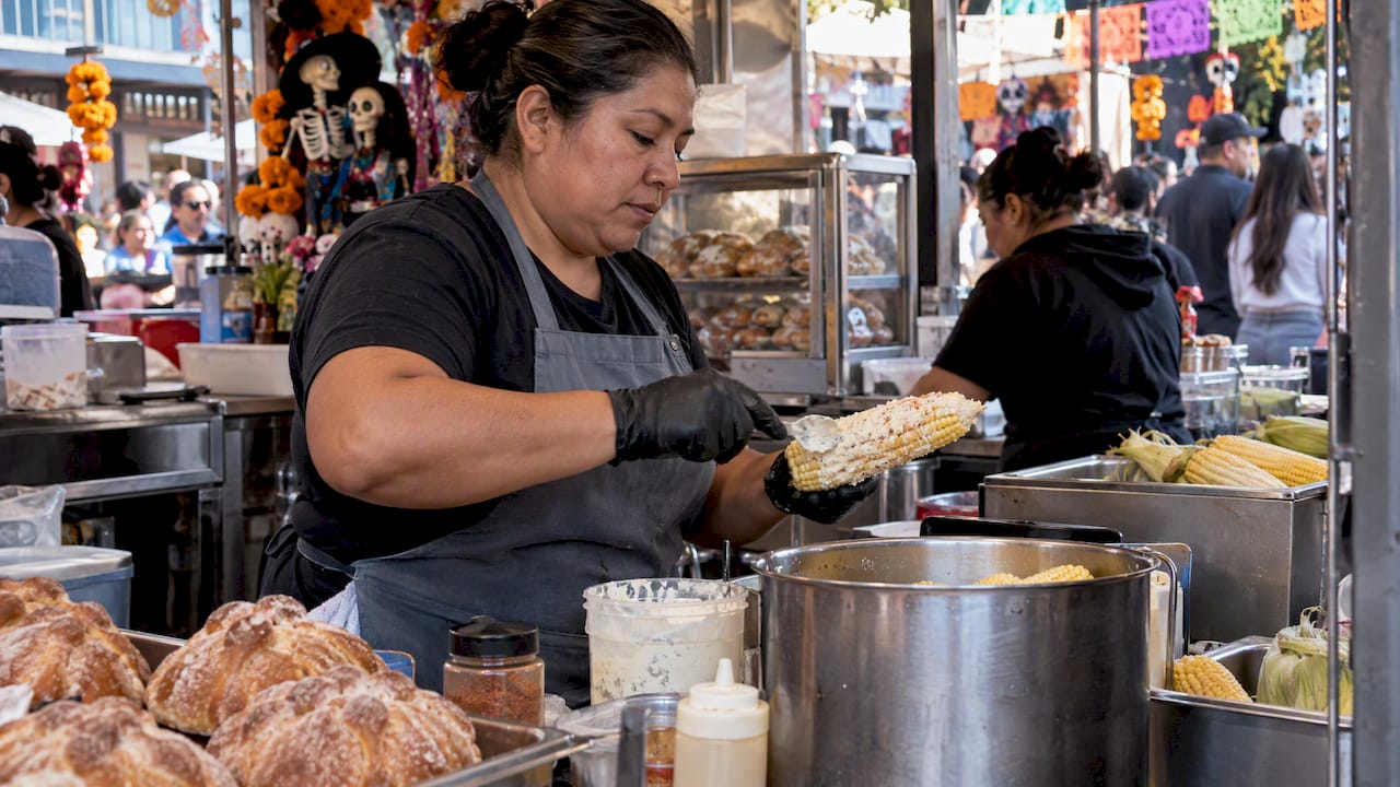 Festival vendor serving elote beside pan de muerto